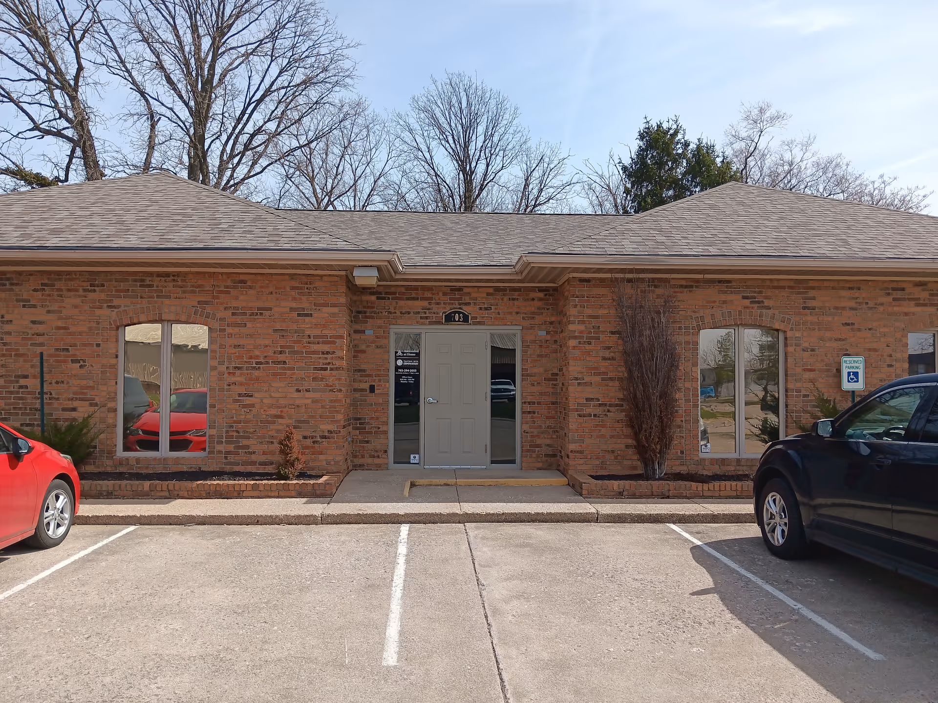 Brick-faced senior living facility front entrance with double doors, parking lot, and leafless trees.