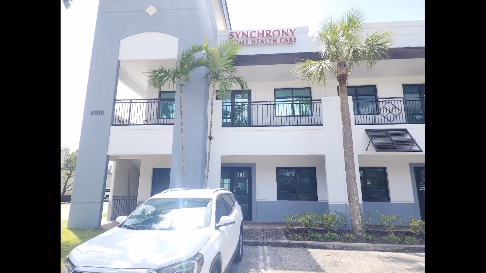 Exterior of Synchrony Home Health Care facility with palm trees and a parked white car.