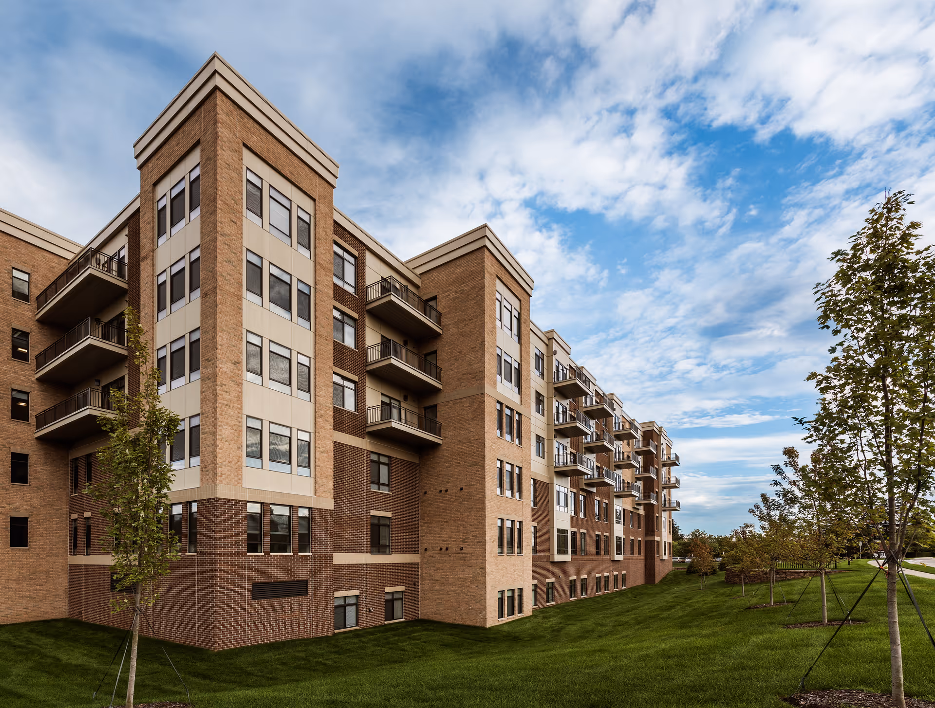 Exterior view of a multi-story senior living building with balconies and green lawn.
