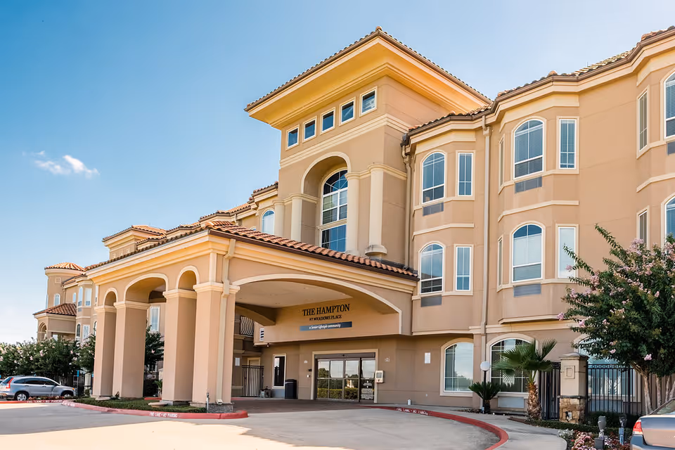 Exterior view of The Hampton at Meadows Place, a peach-colored senior living building with arches.