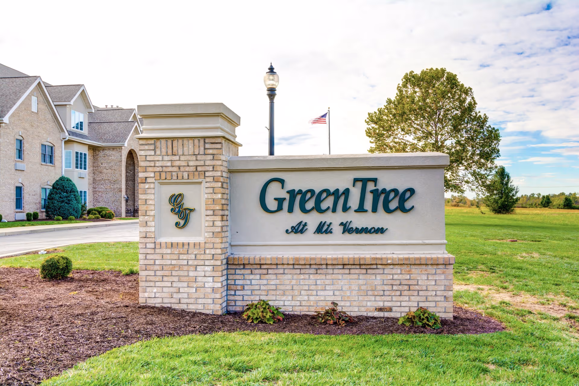 A brick entrance sign reading 'GreenTree At Mt. Vernon' stands on a grassy lawn outside a multi-story senior living building.