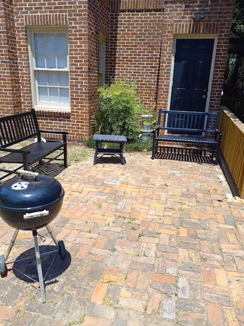 Outdoor brick patio with benches, a grill, and a doorway to a senior living home.