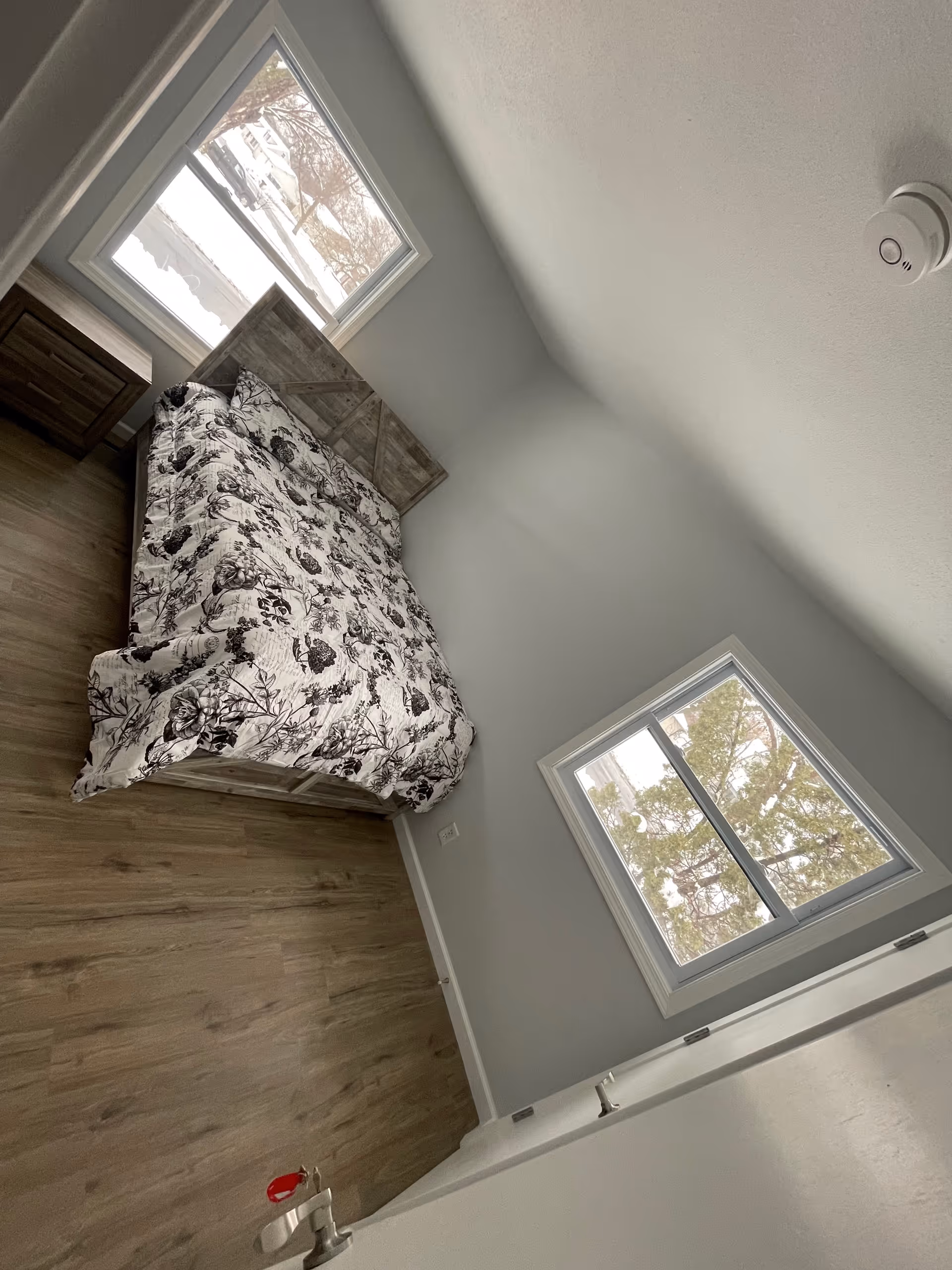 A cozy bedroom with a floral-patterned bed, two windows, and neutral gray walls.