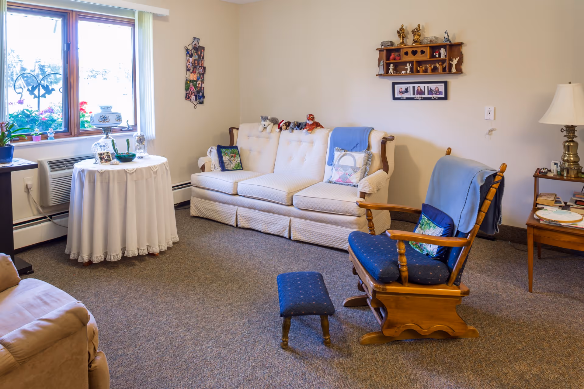 Cozy living room with sofa, rocking chair, ottoman, lamp, and window seating.
