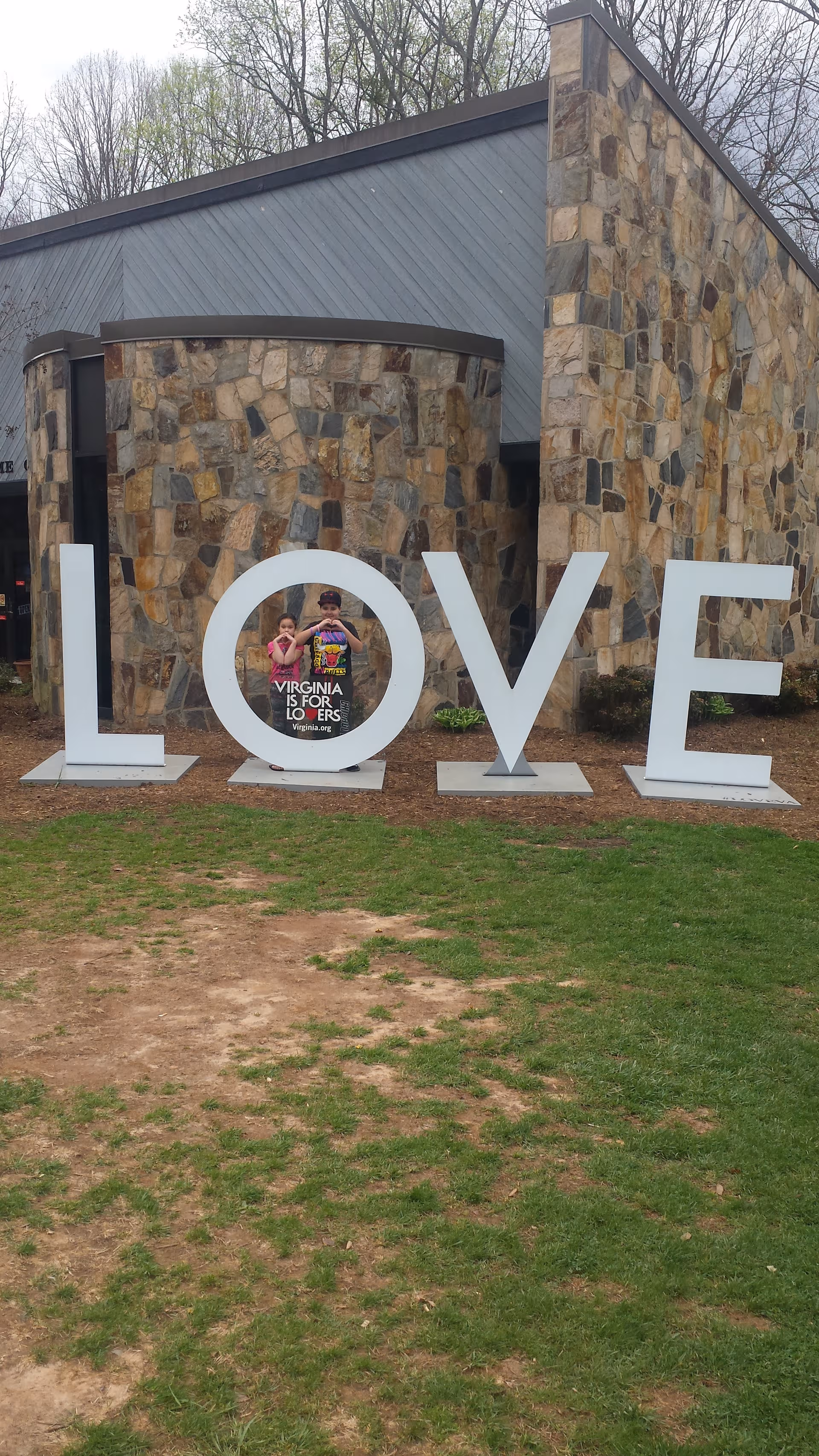 Large white LOVE letters in front of a stone building; two children peek through the O.