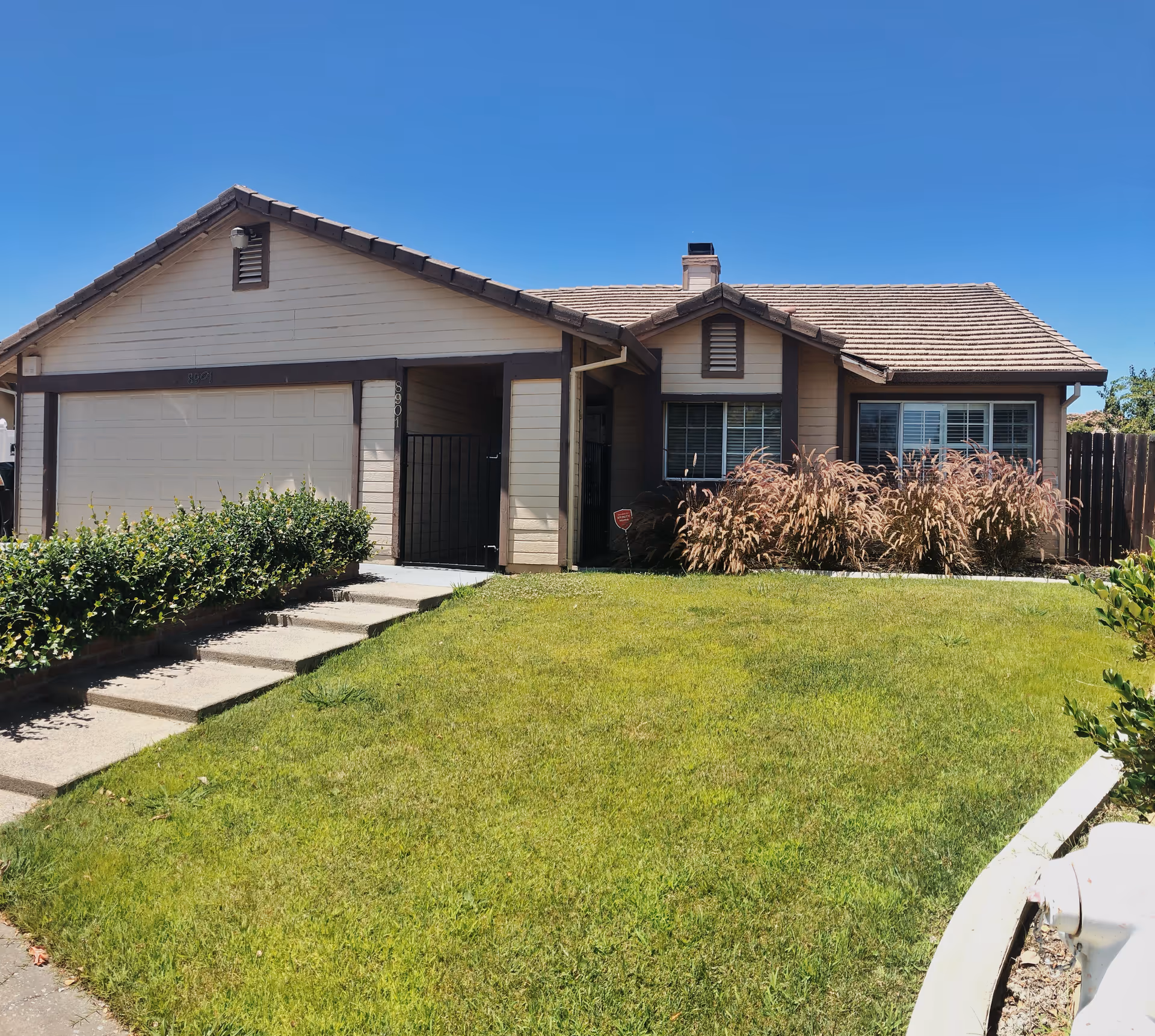 A single-story suburban house with a manicured lawn, front steps, and gated entrance.