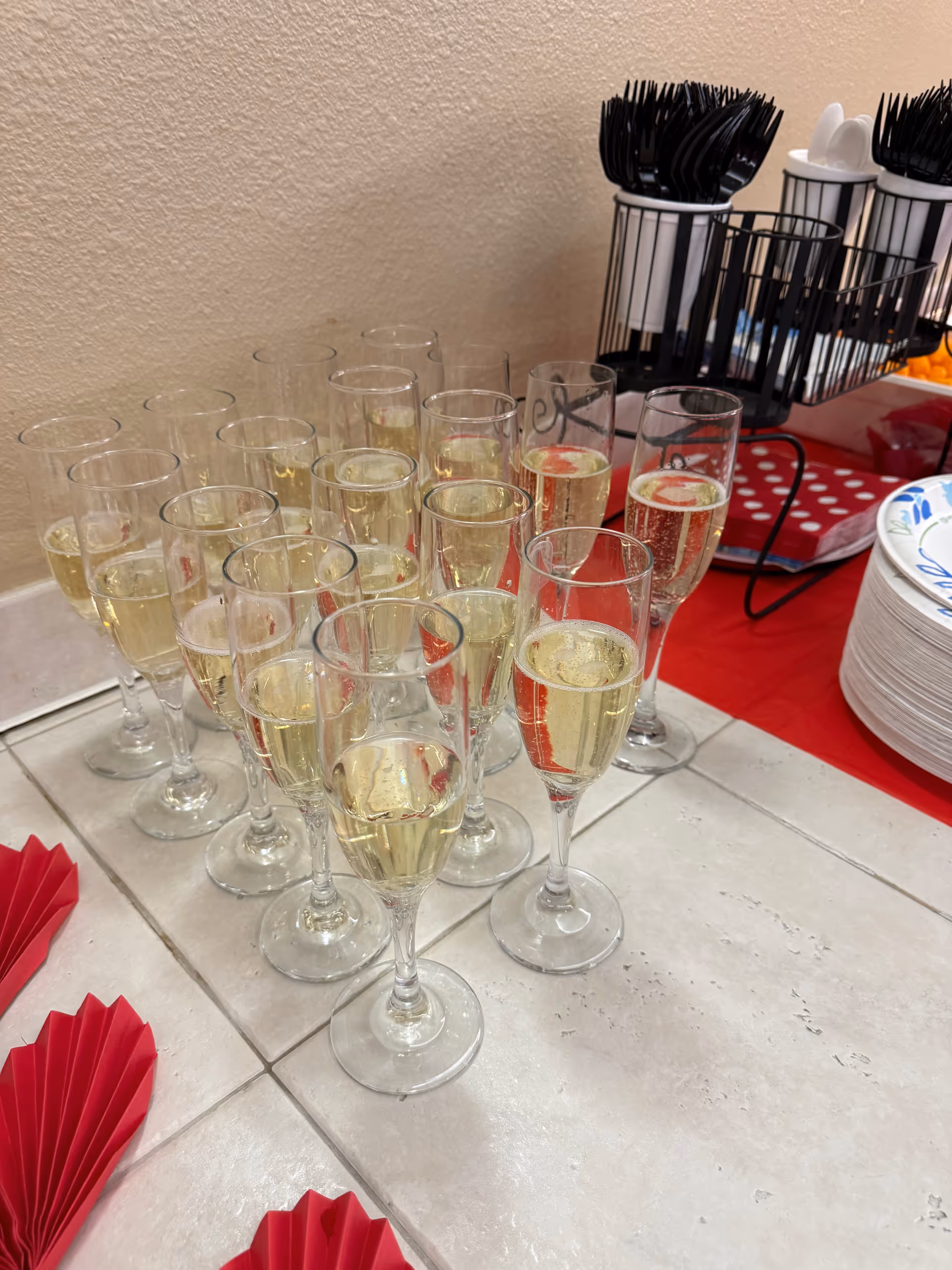 Rows of champagne flutes on a tiled table with red napkins.