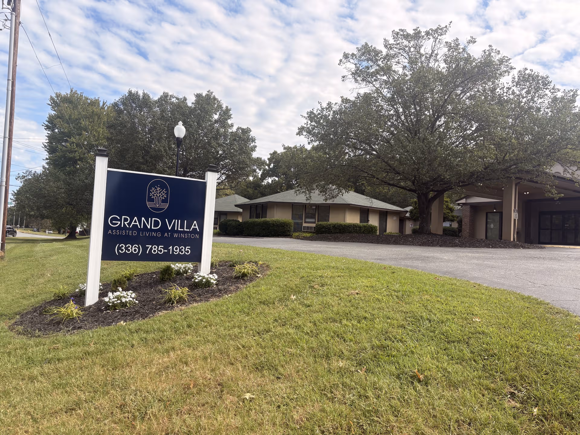 Blue Grand Villa sign on a landscaped lawn with a beige building entrance behind.