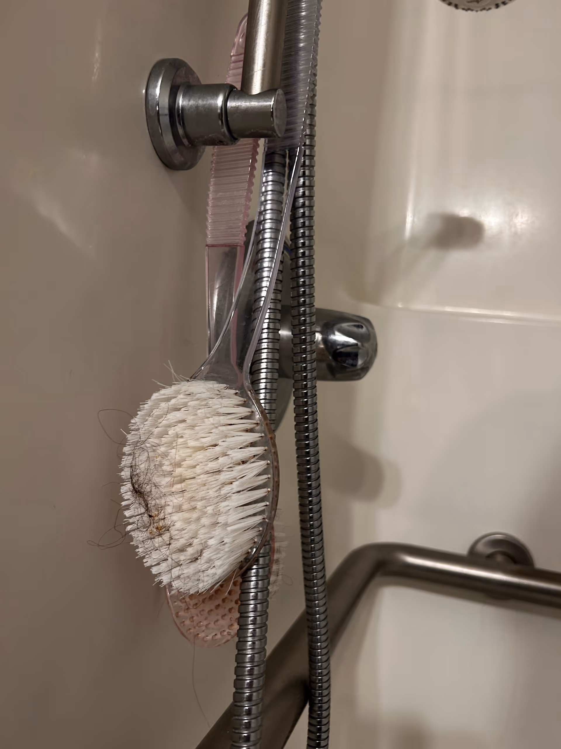 Bathroom shower area featuring a handheld shower, hairbrush tangled among hoses, and a grab bar.