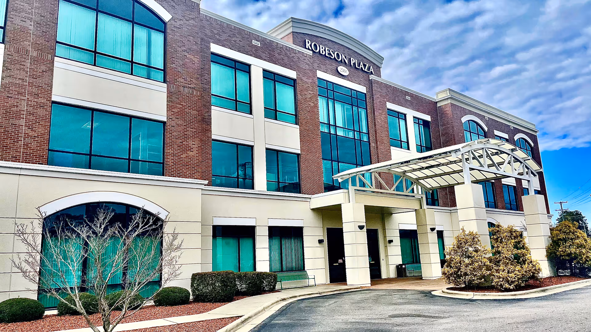 Brick medical facility exterior with teal windows and a curved glass entrance canopy.