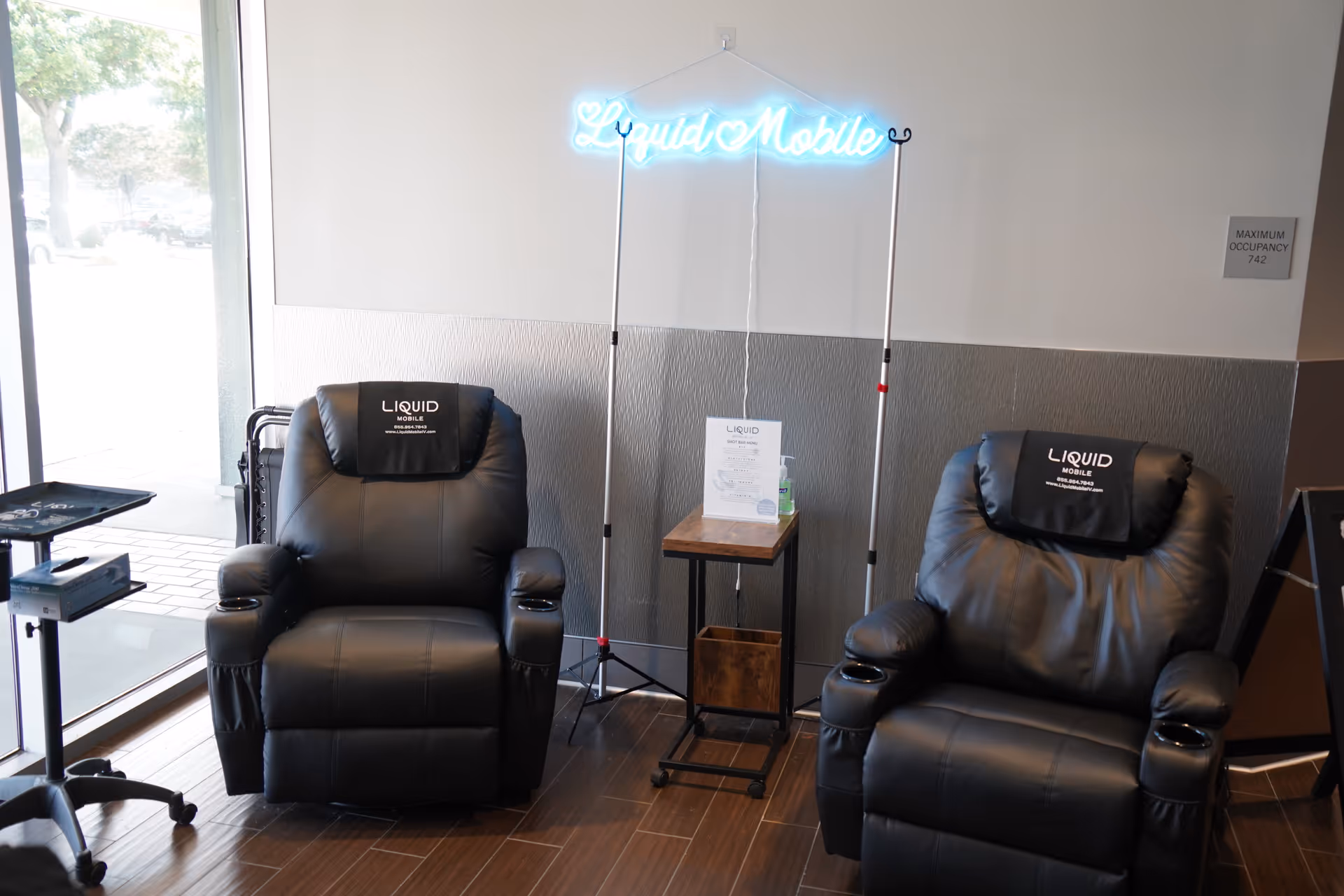 Two black leather recliners beside a small table and neon sign in a modern lounge.
