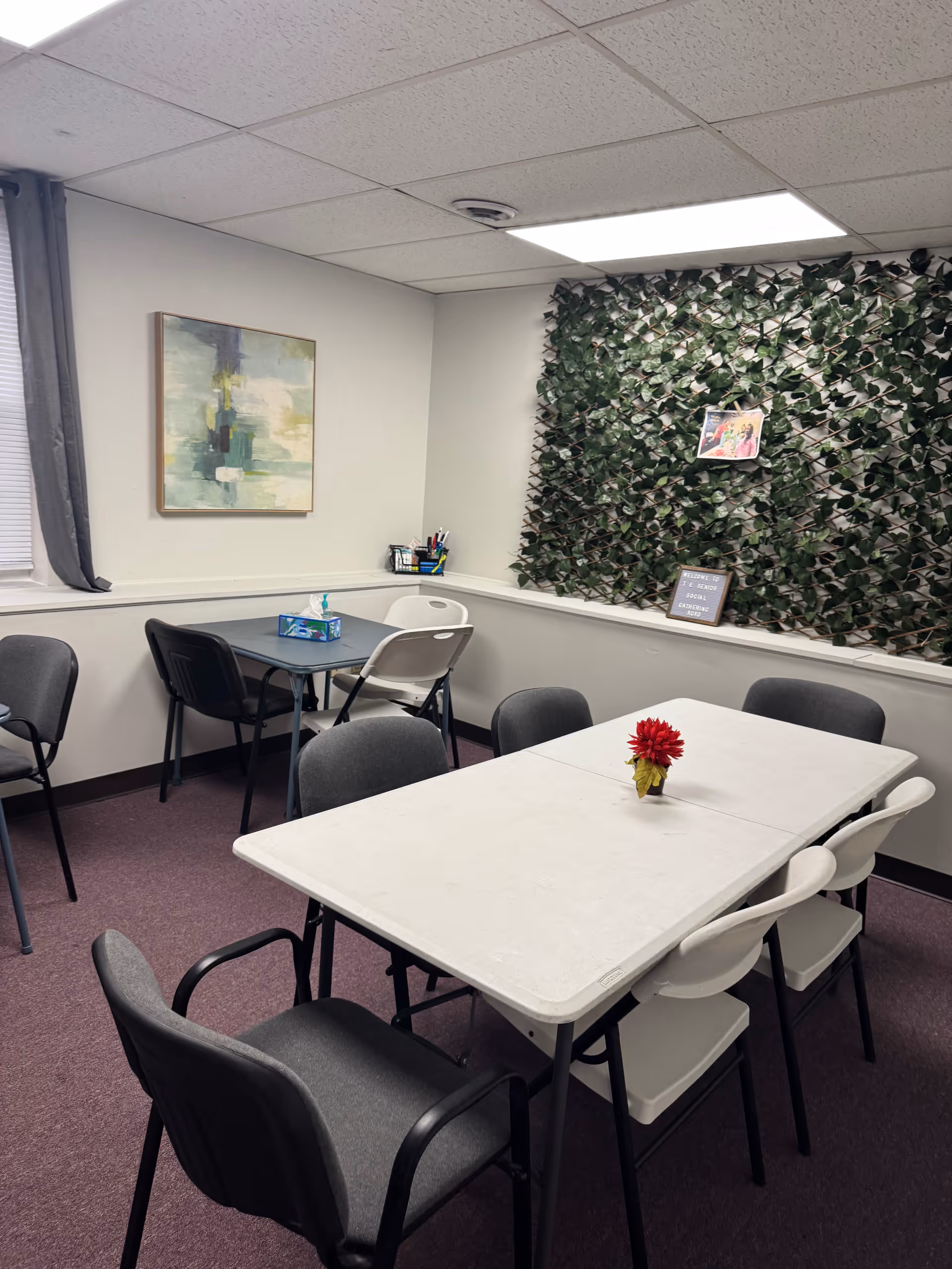 Interior of a small dining area with tables, chairs, and a leafy wall decor.