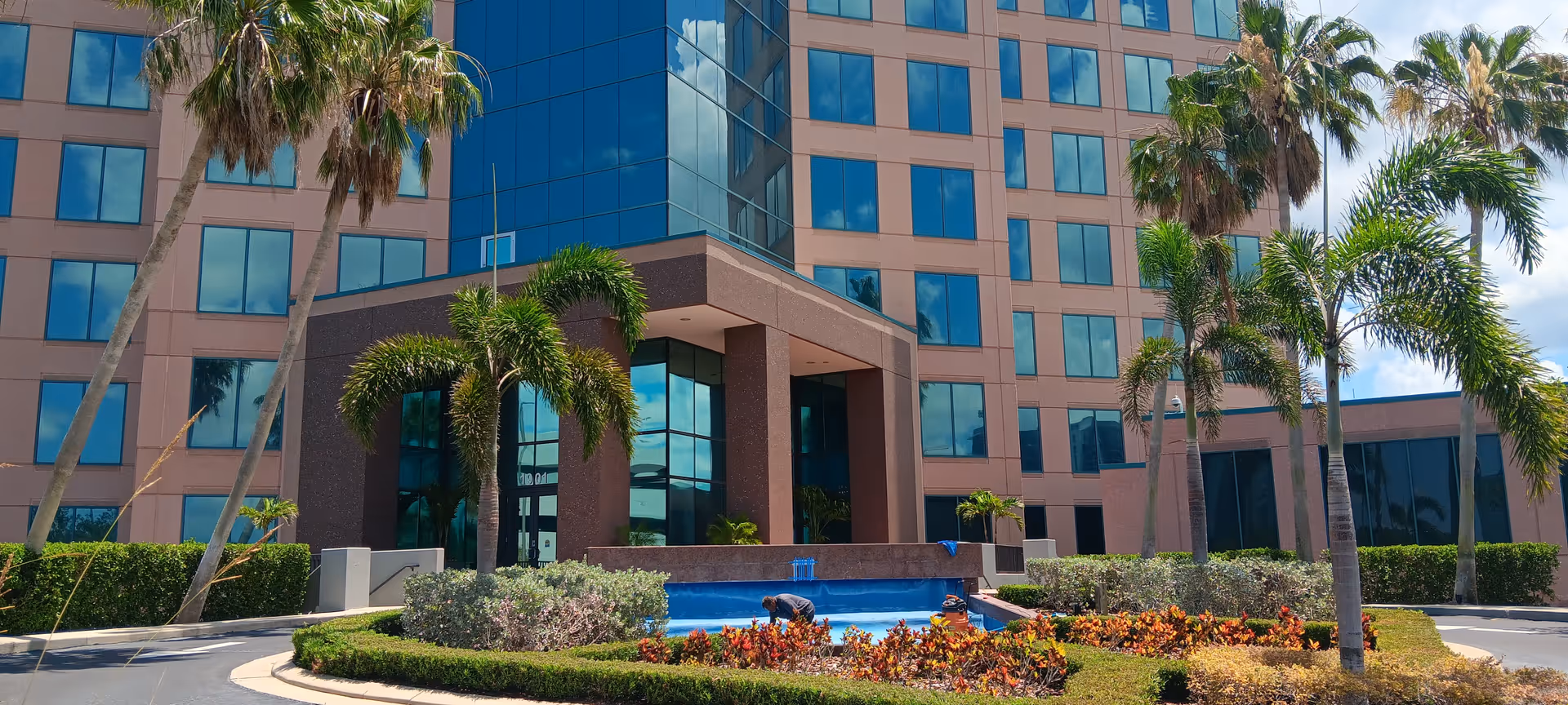 Modern multi-story senior facility with pink facade, palm trees, and a front entrance courtyard.