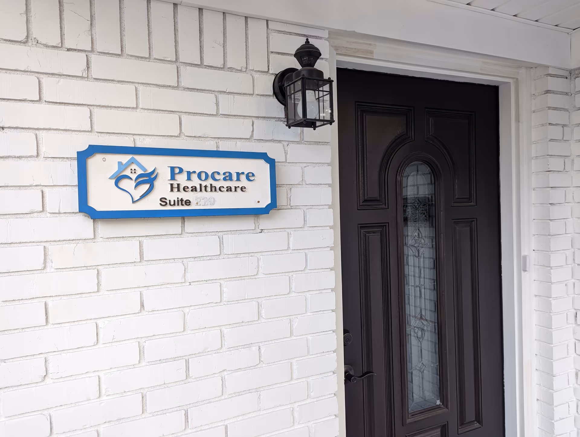 White brick exterior with Procare Healthcare sign and dark ornate front door entrance.