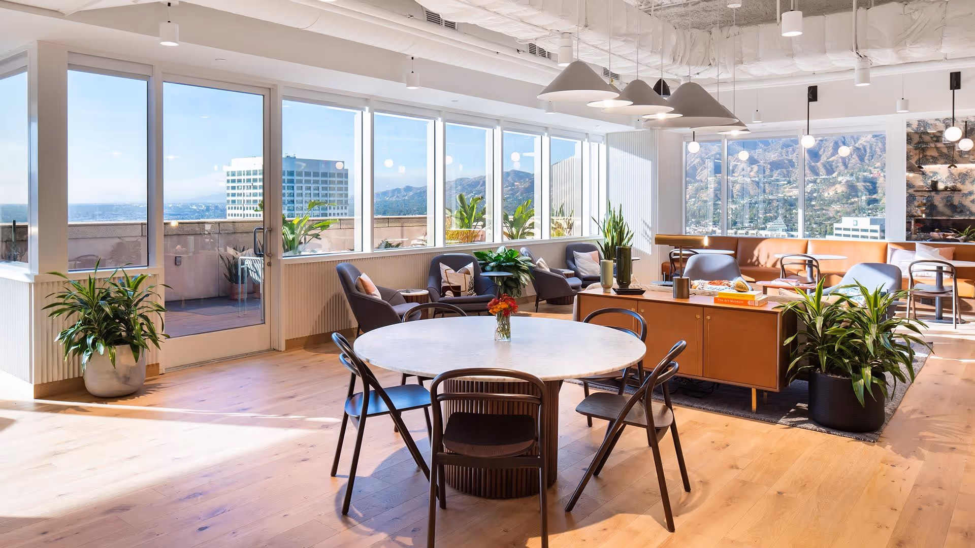 Bright open lounge area with round table, chairs, couches, plants, and large windows.