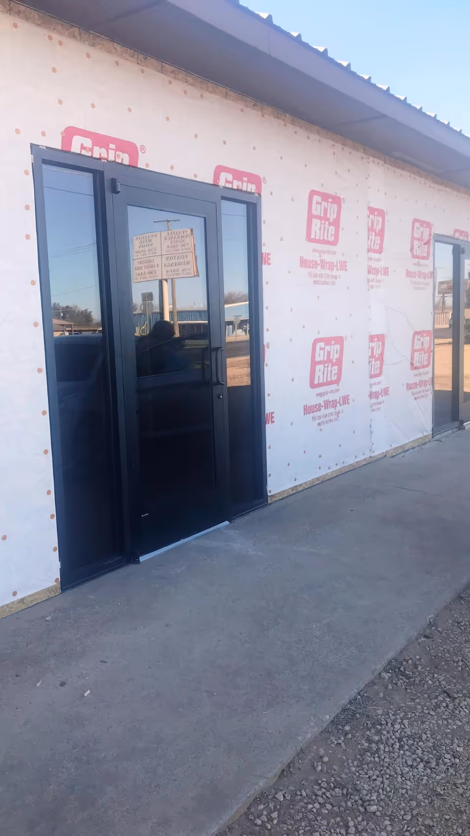 Exterior view of a building under construction with glass doors and wrapped walls.