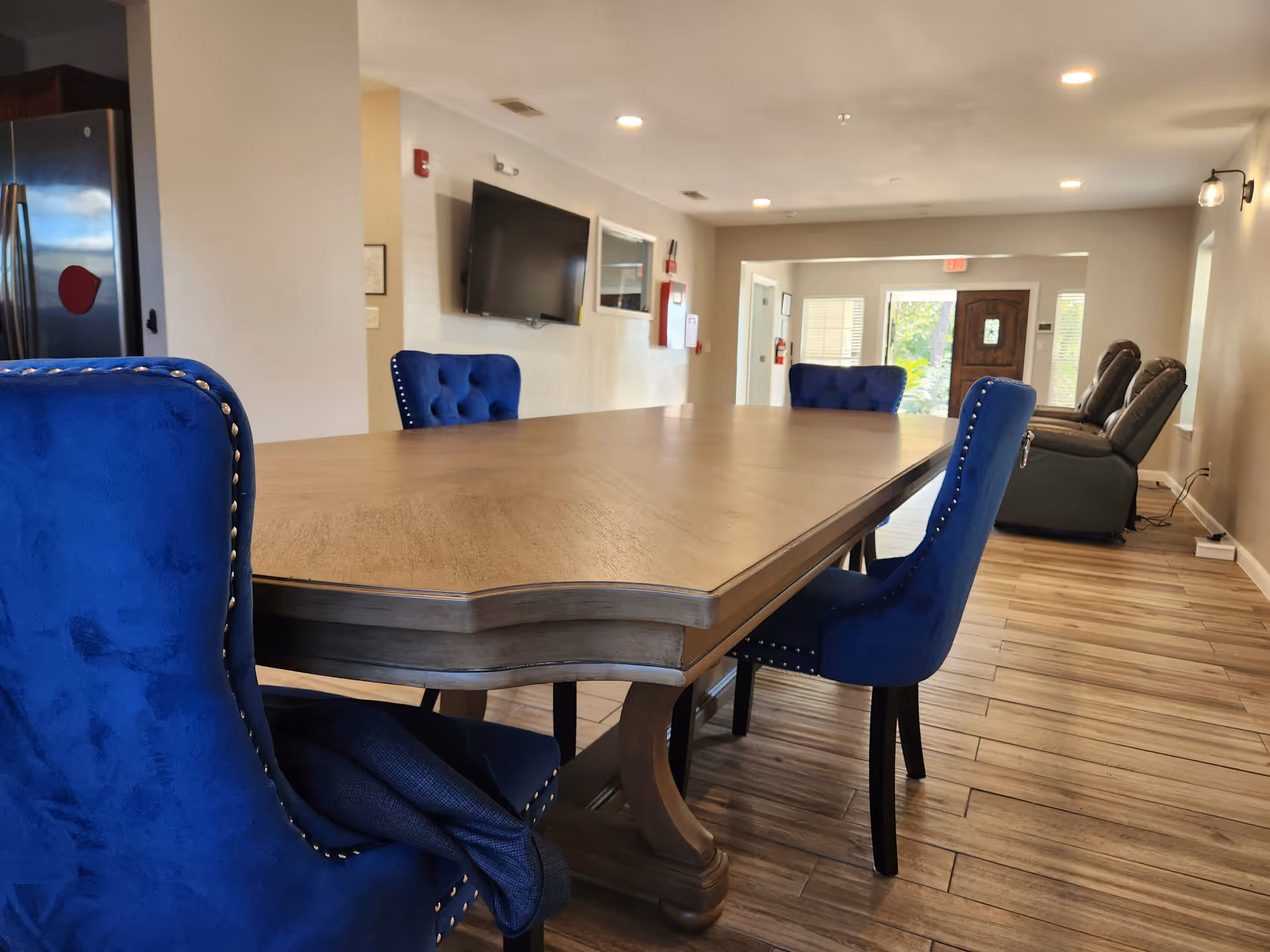 A large wooden dining table with blue upholstered chairs in a bright lounge area.