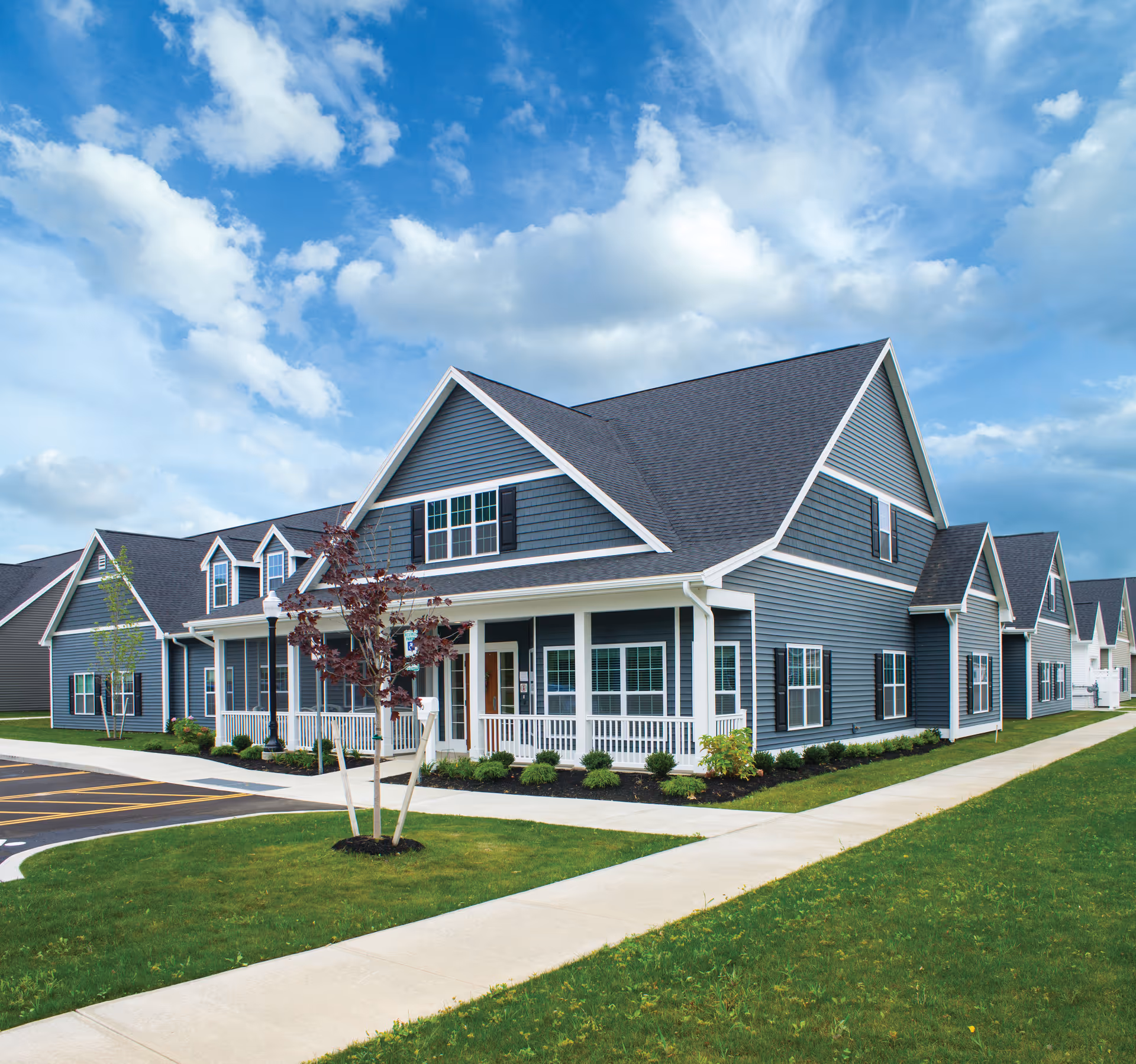 Row of blue-gray senior living townhouse buildings with porches and manicured lawns.