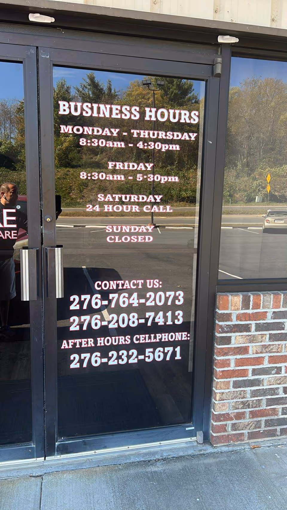 Glass storefront door displays business hours and contact numbers.