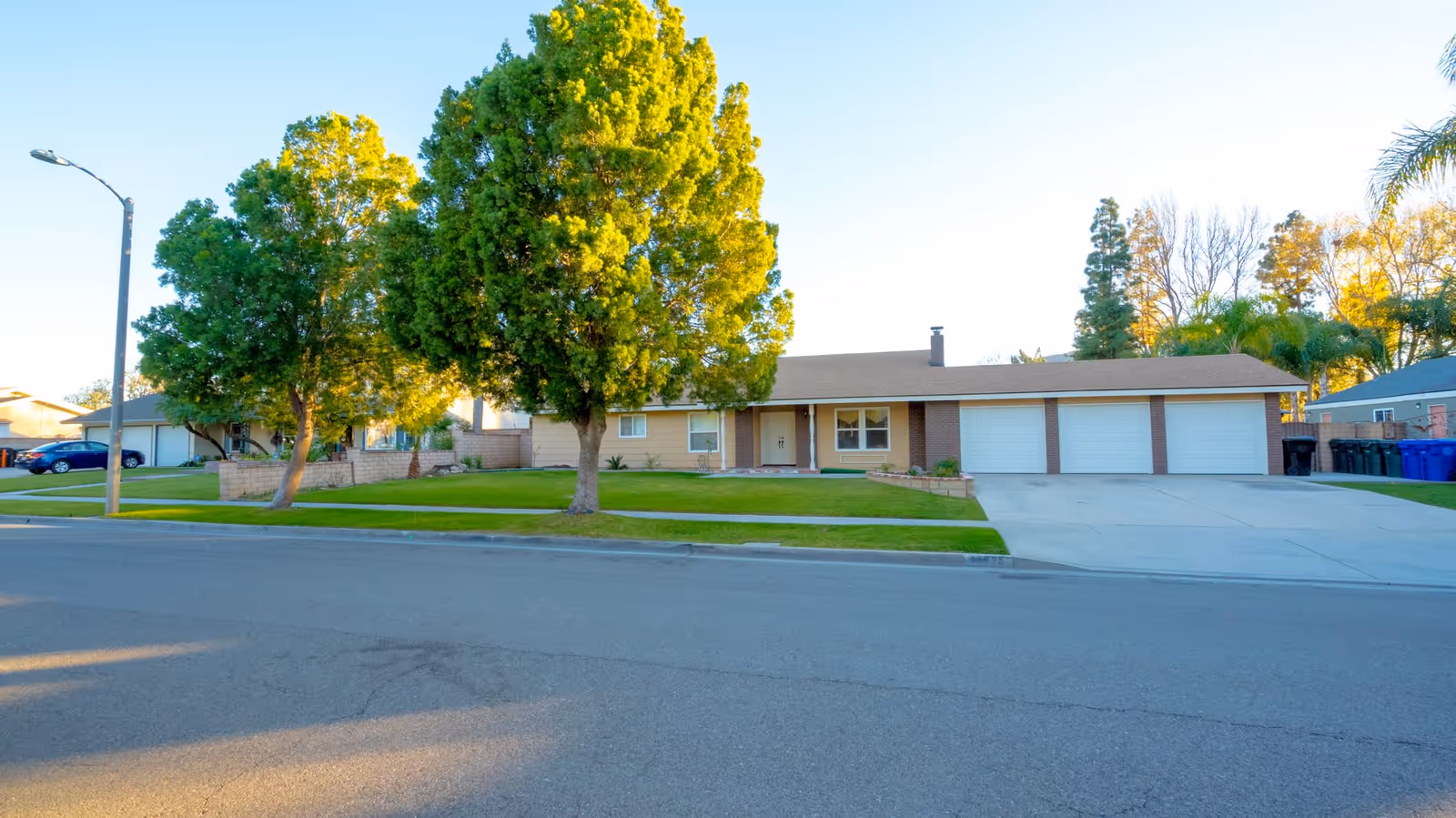 Single-story suburban house front with a wide driveway, three-car garage, lawn and trees.