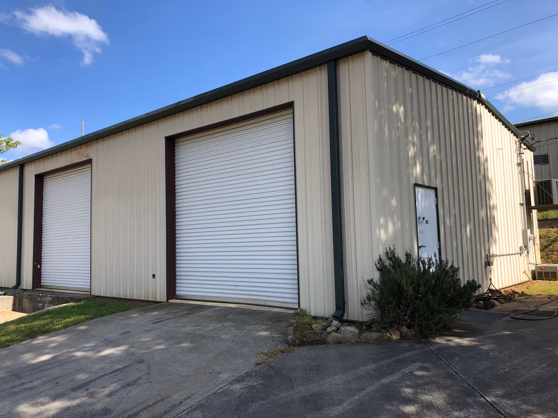Exterior view of a beige metal building with large white roll-up doors and driveway.