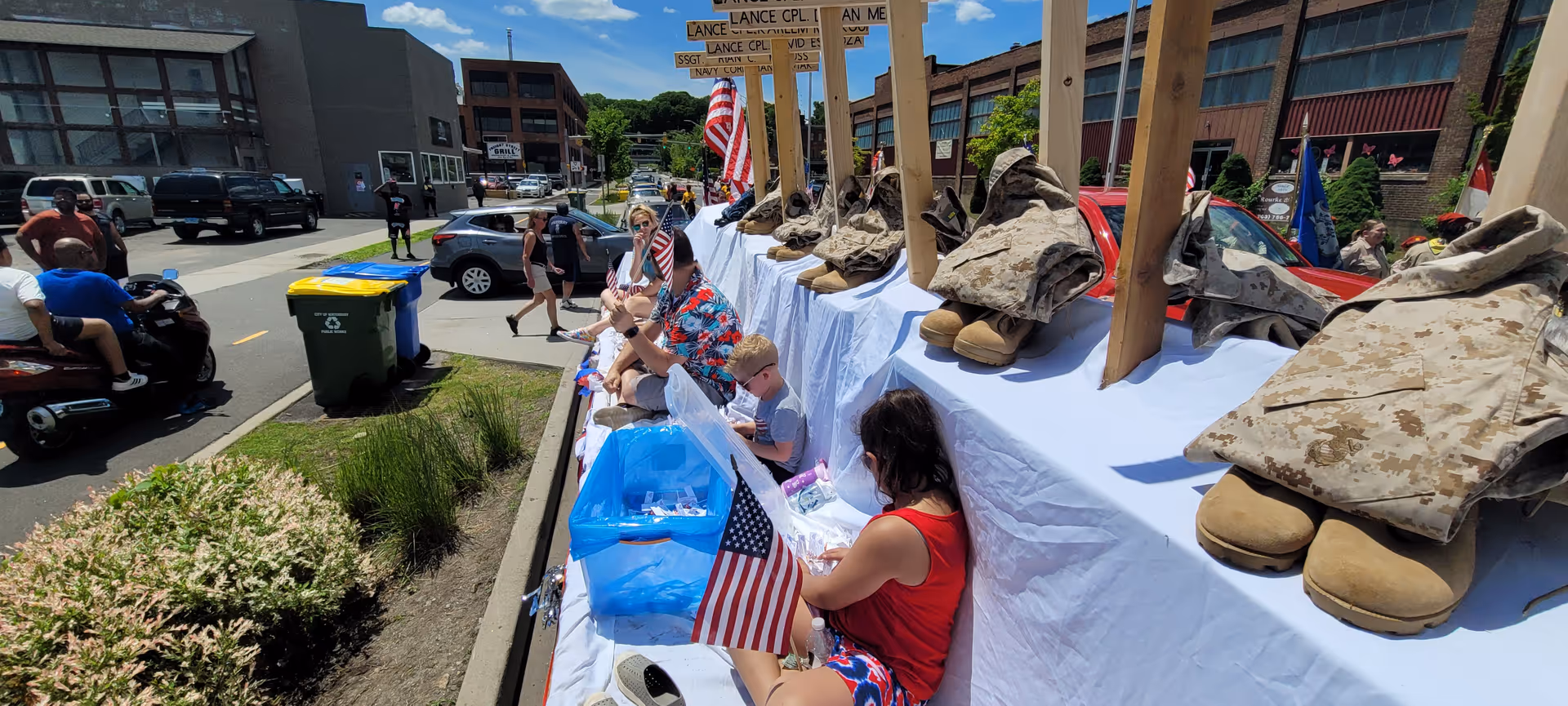 Outdoor street display of military boots along a long table with people nearby.