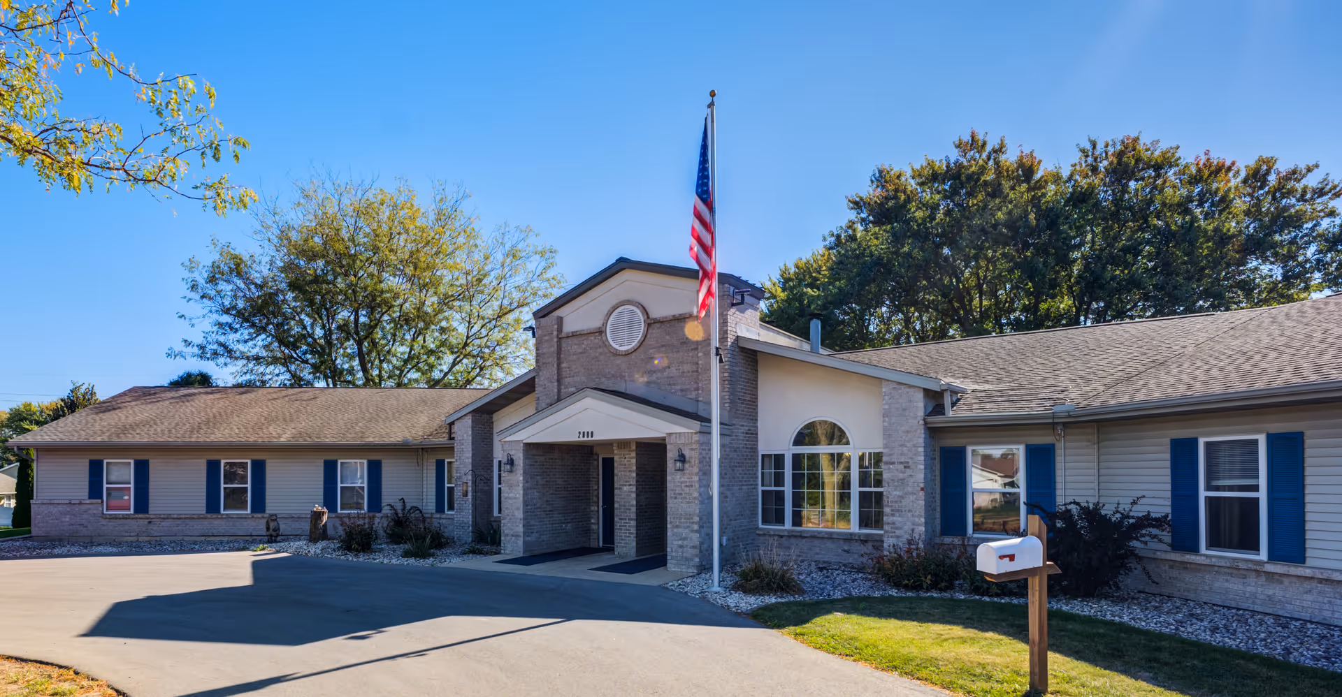 Exterior view of a single-story senior living facility with flagpole and brick accents.
