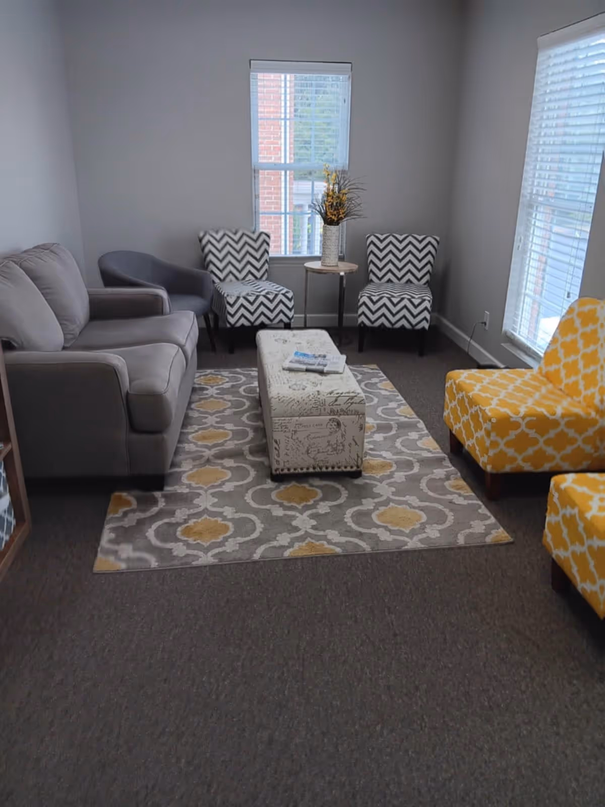 Cozy living room lounge with gray sofa, patterned chairs, rug, and natural light.