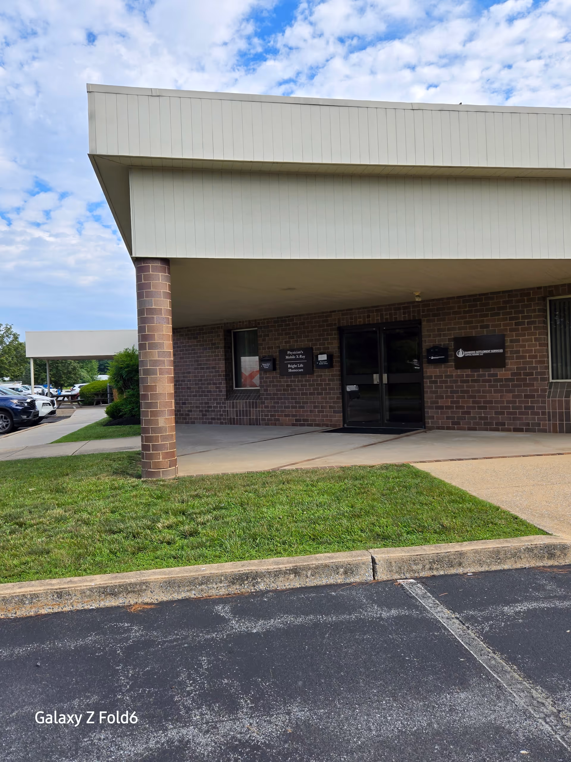Brick building entrance with a beige overhang and a parking lot nearby.