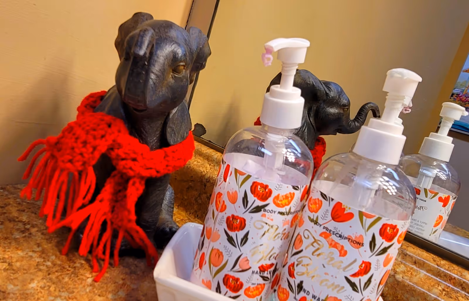 Decorative elephant figurines with red scarves beside floral hand soap dispensers on a counter