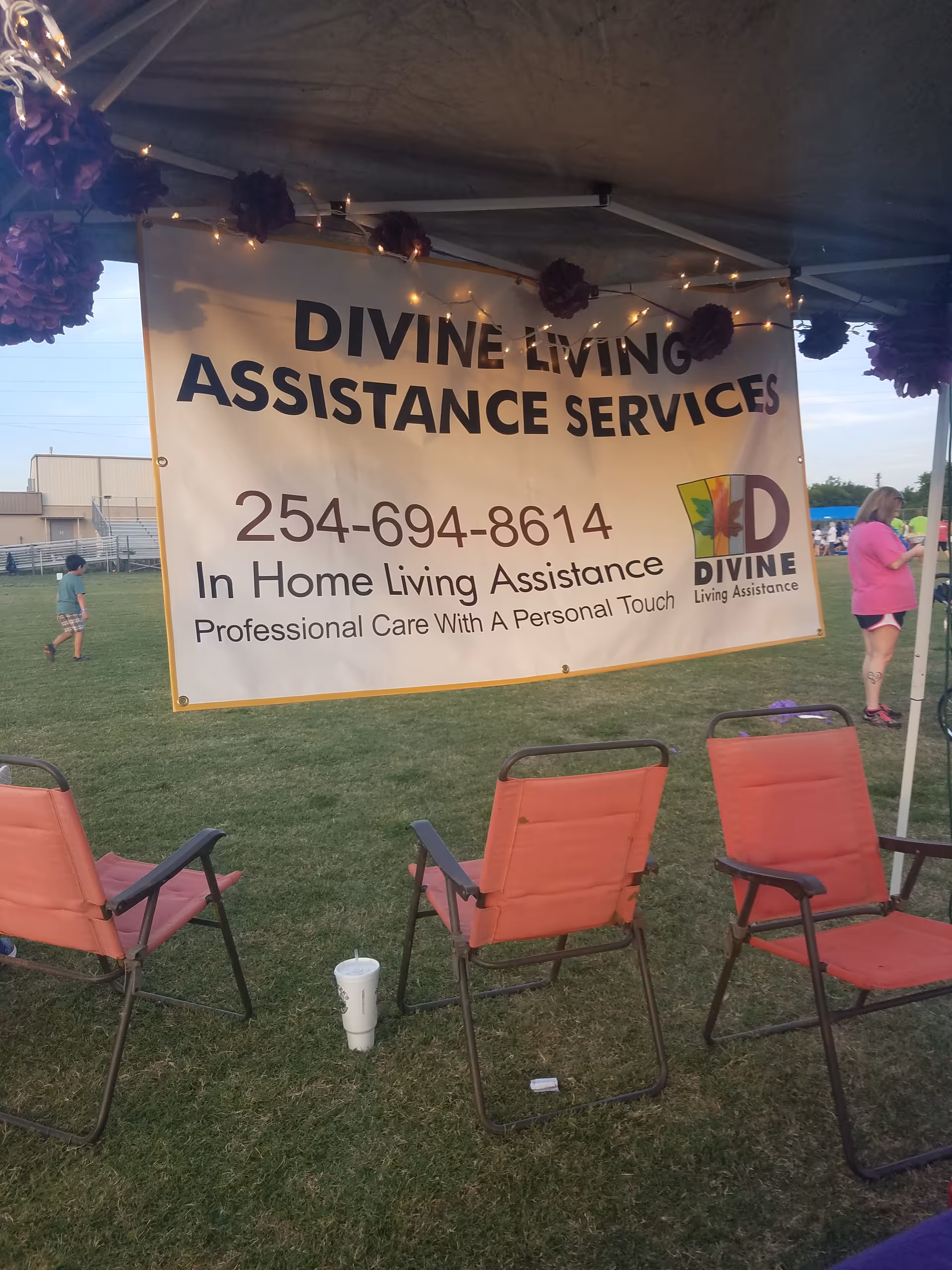 Outdoor tent with a large banner reading Divine Living Assistance Services and chairs.