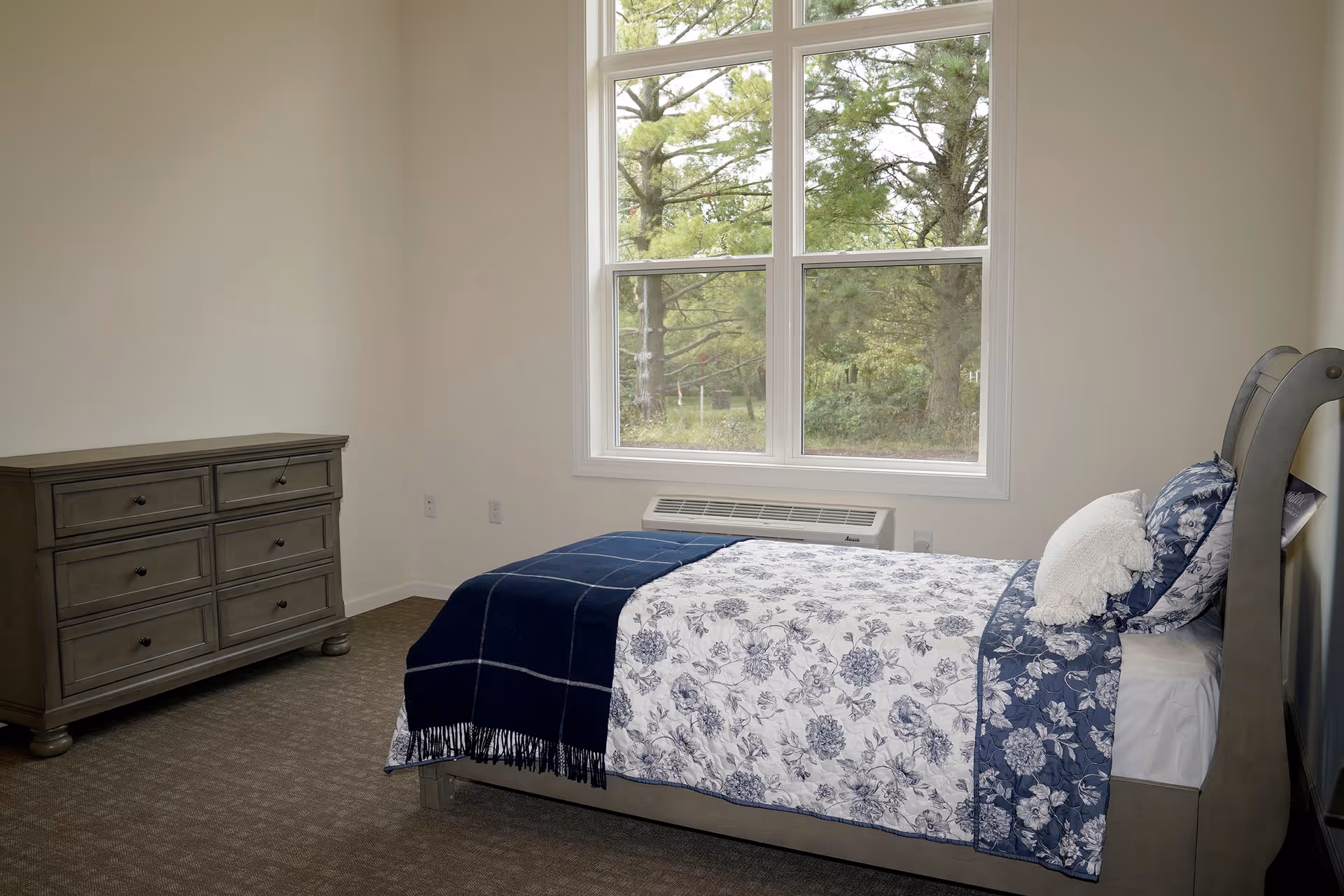 Bedroom in Anita's Gardens of Brookfield with floral bedding, dresser, and window.
