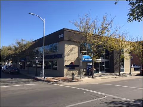 Corner street view of a beige commercial building with glass windows and trees.
