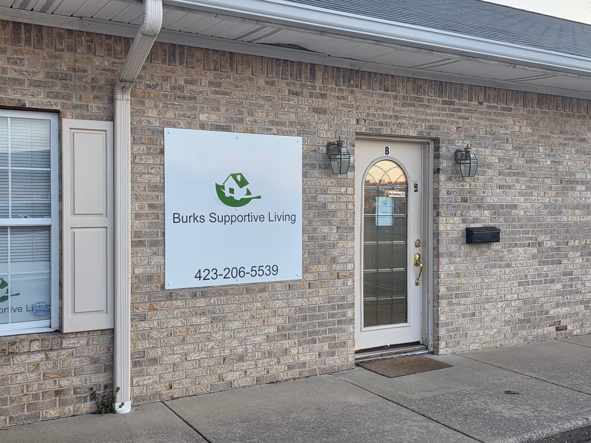 Brick exterior of Burks Supportive Living with a glass door entrance and sign.