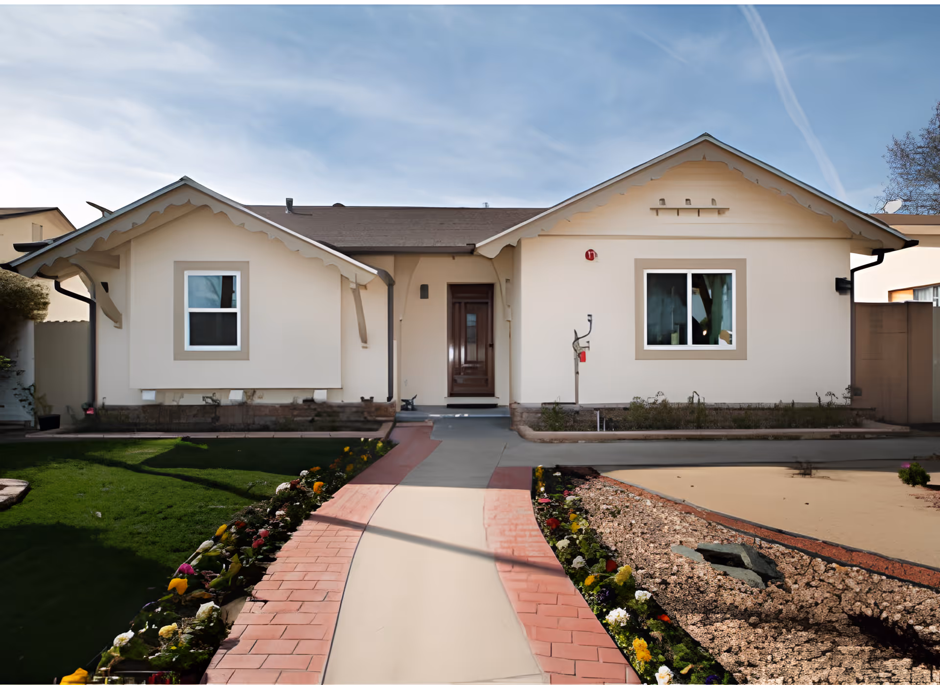Front exterior of a single-story cream-colored house with a central walkway and landscaped flower beds.
