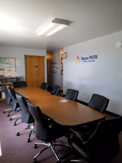 Interior conference room with a long table, chairs, and Nexus-PATH Family Healing logo.