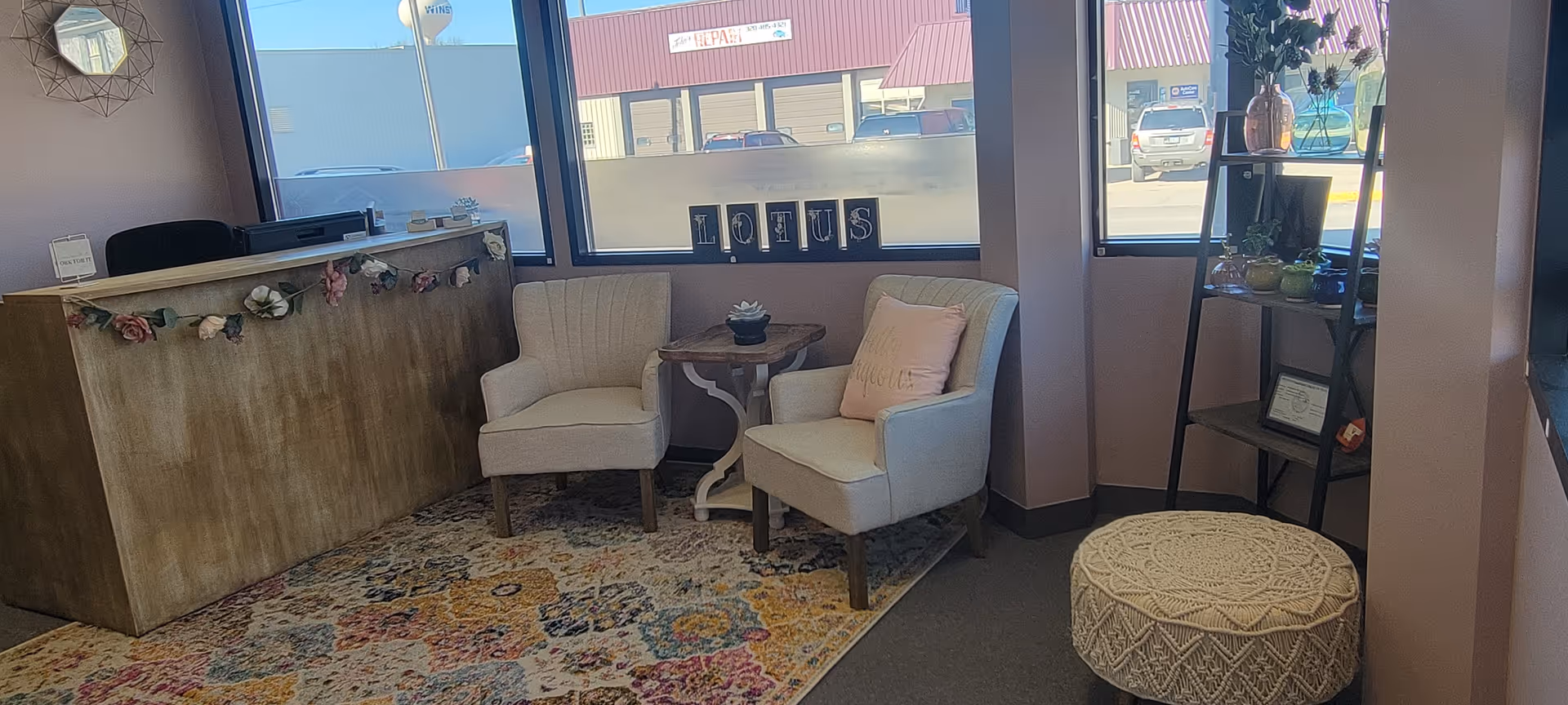 Reception area with two white chairs, a small table, and a floral garland near the counter.