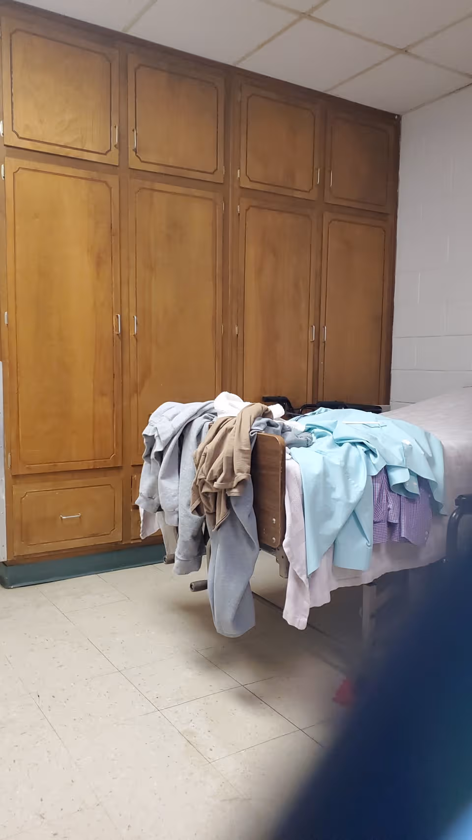 Tall wooden cabinets line a room with a bed covered in clothes.