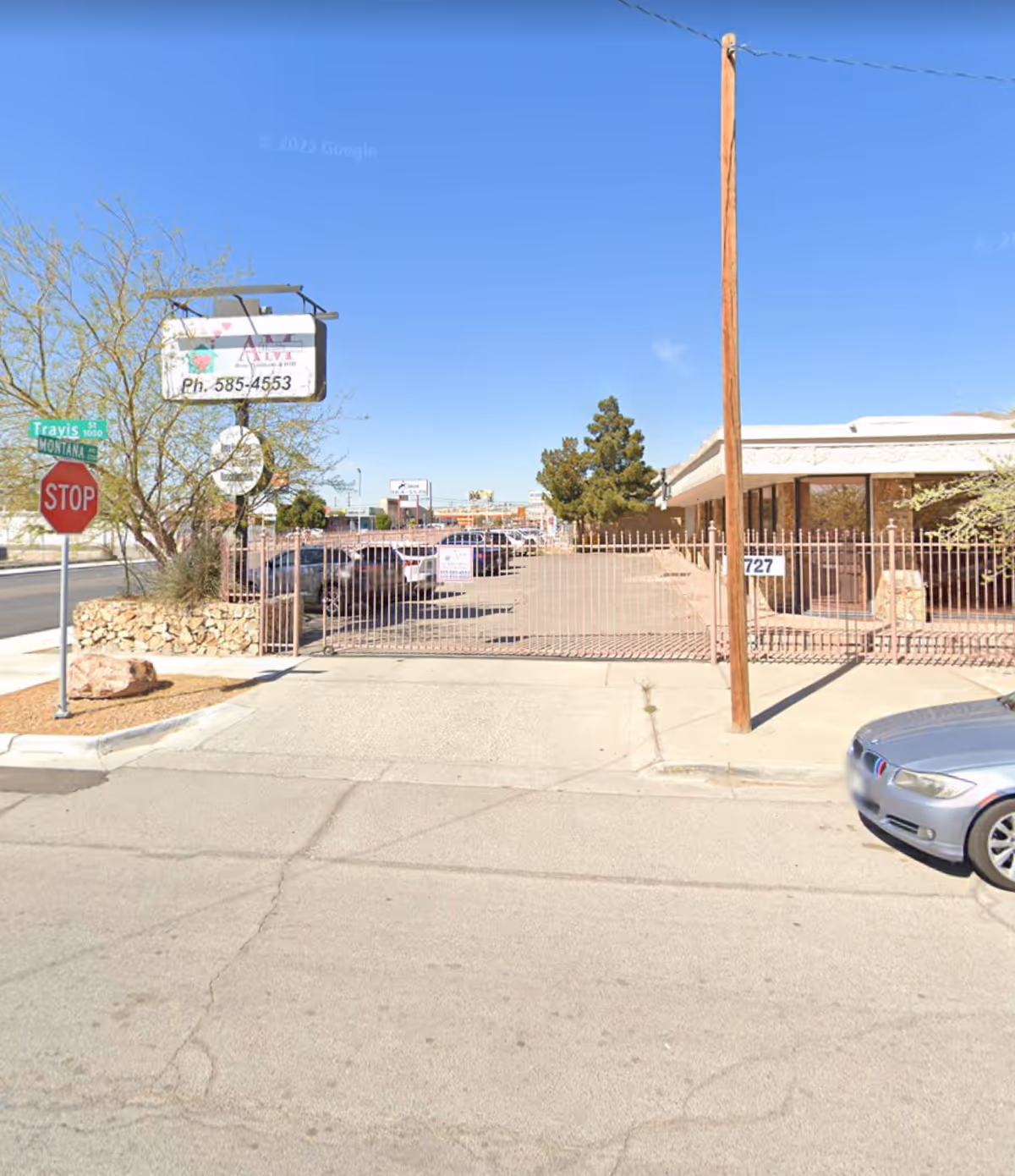 Sunlit exterior view of a gated senior living facility entrance with parked cars nearby