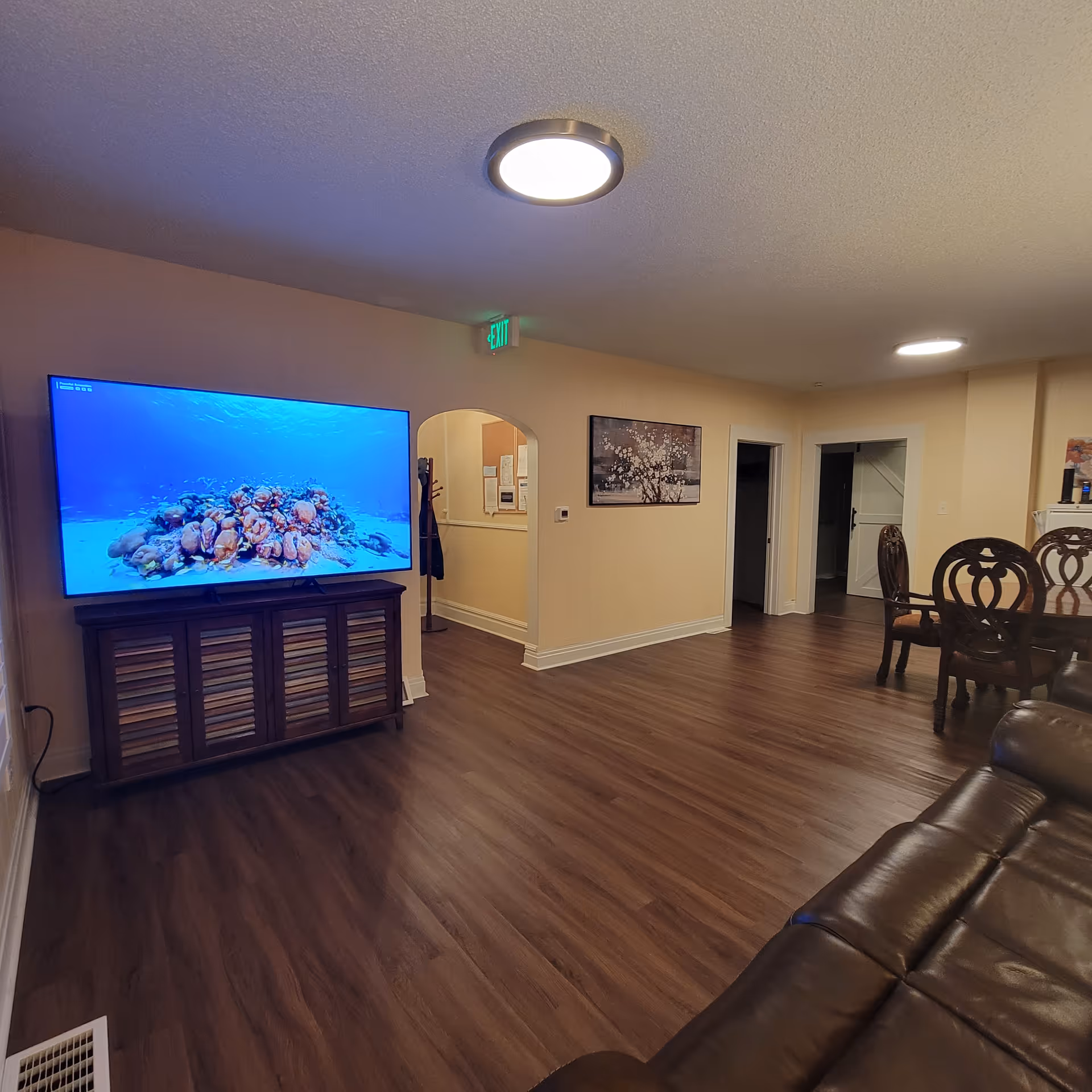 Living room in a senior living facility featuring a large TV, leather sofa, and dining set.