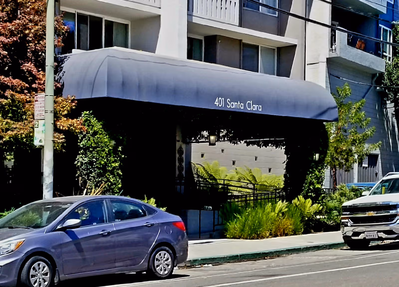 Exterior building entrance with a blue awning reading 401 Santa Clara and surrounding greenery