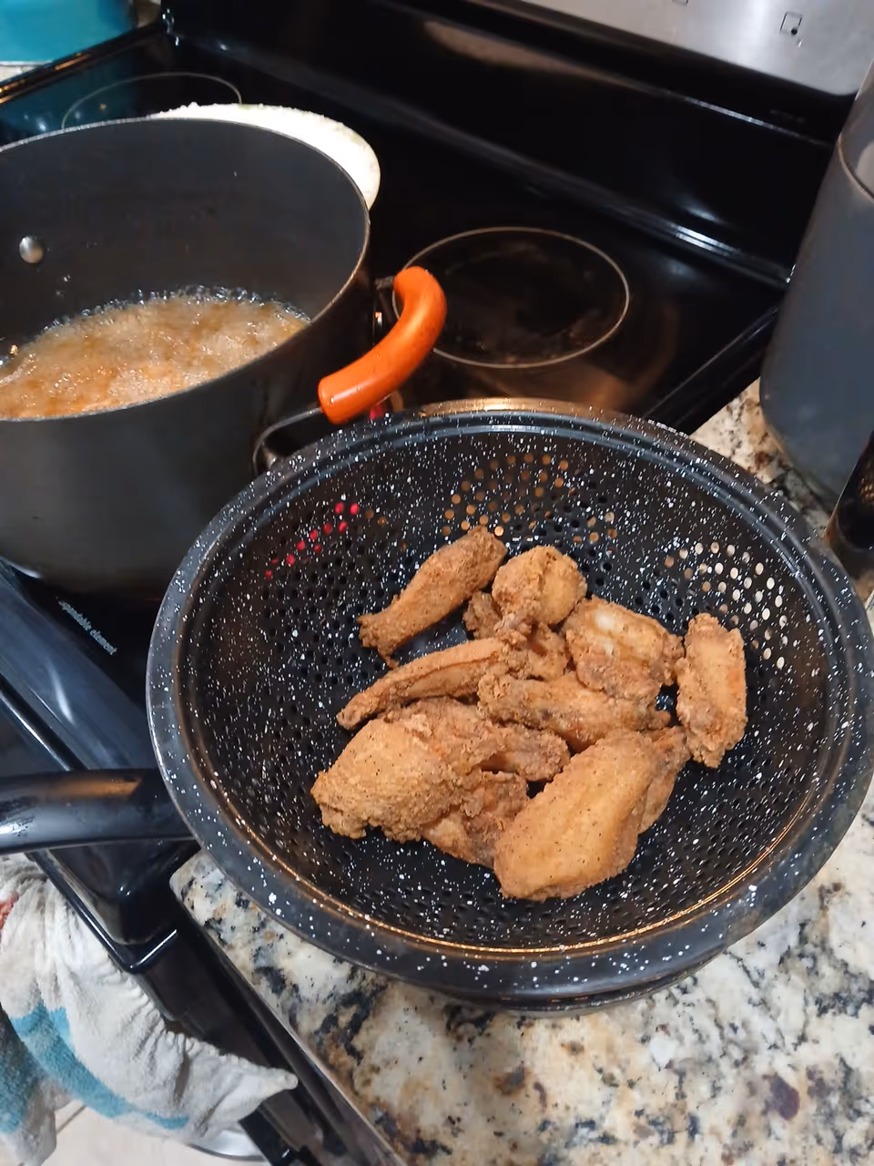 Frying basket with breaded chicken beside a boiling pot on a kitchen stove.
