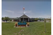 Front view of The Meadows senior living facility with flag, sign, lawn, and parked cars.