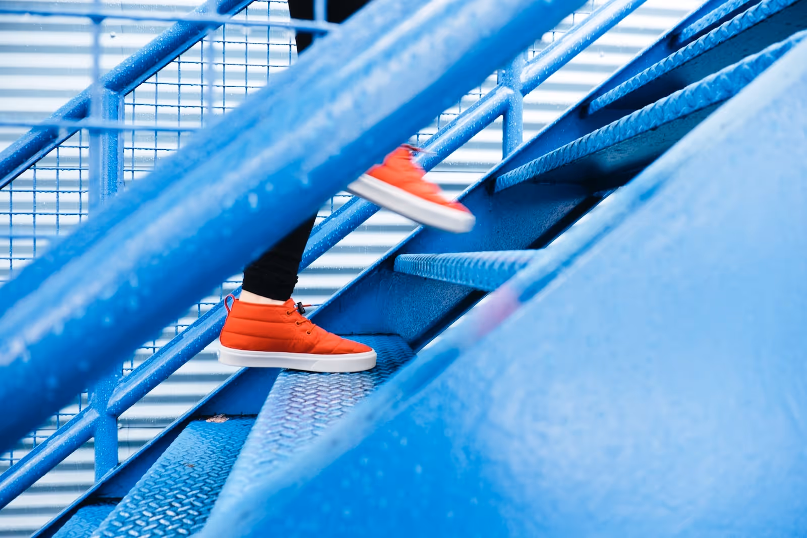 Close-up of blue metal exterior stairs with a person wearing red sneakers.
