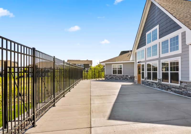 Exterior view of Suite Living Senior Care of Maple Grove with a walkway and fence.