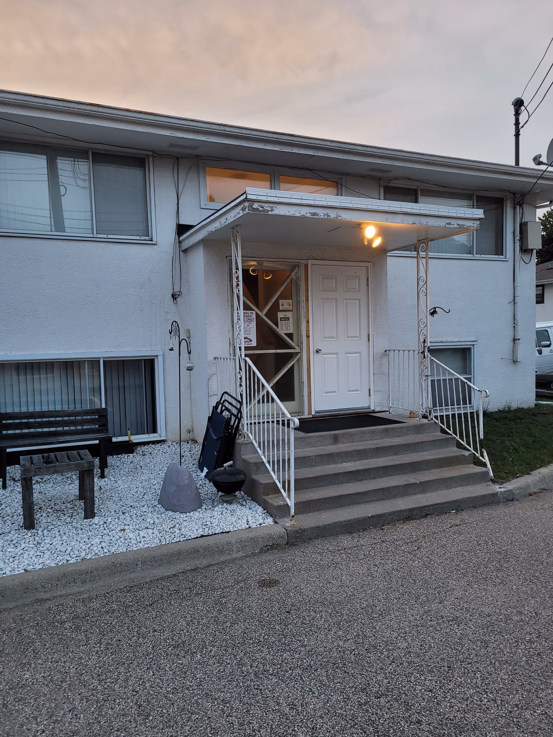 Exterior entrance of a small building with stairs, railing, and a parked bench outside.