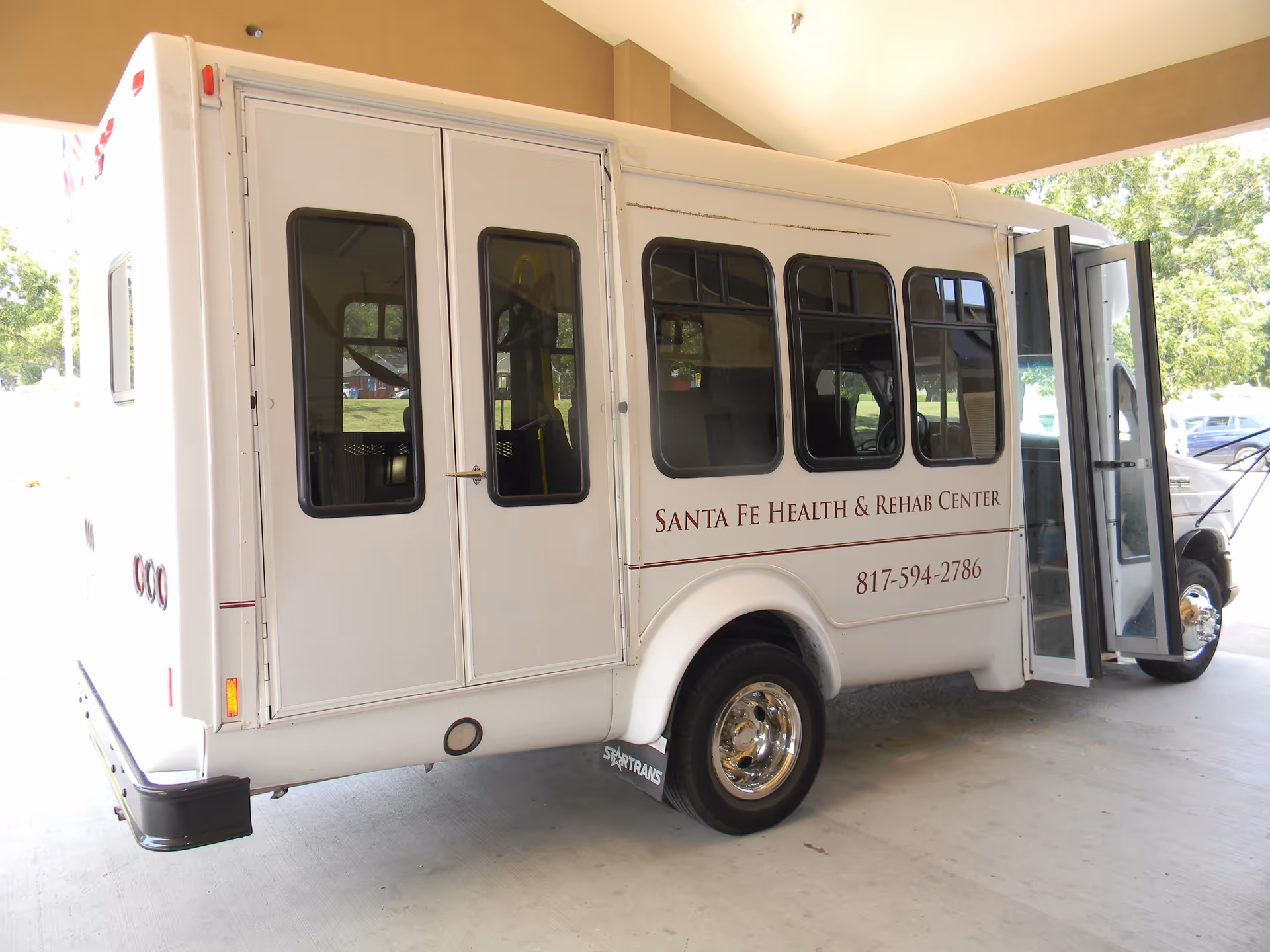 A white shuttle bus with open door parked at Resthome under a covered area.