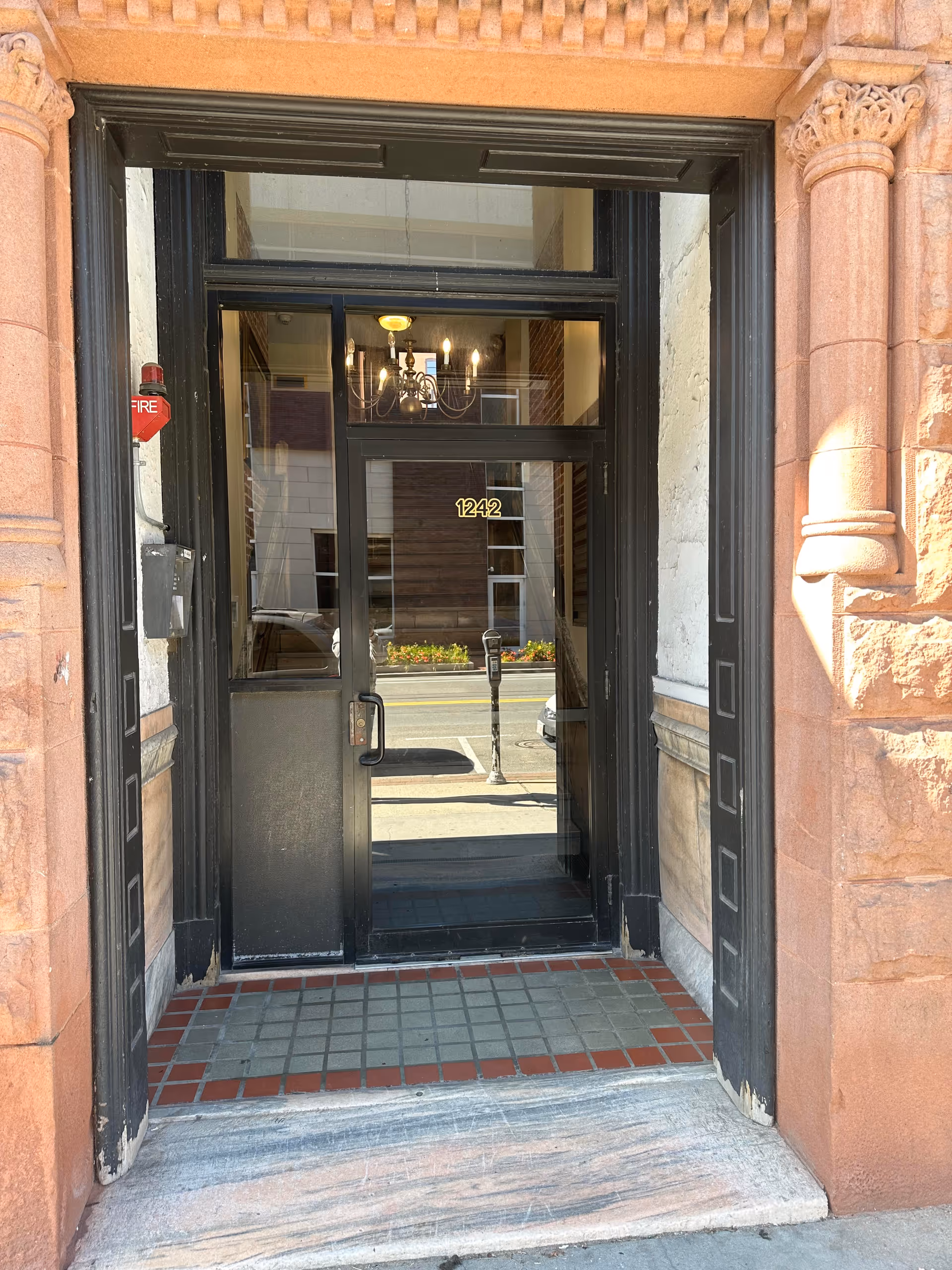 Exterior brick building front with black glass doorway and chandelier visible through the entrance.