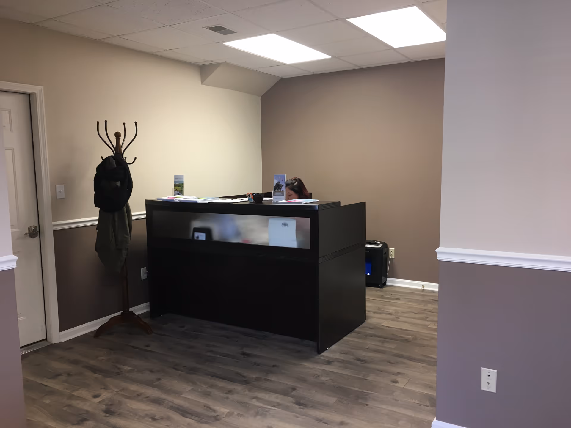 Reception desk in a neutral-toned lobby with coat rack and staff