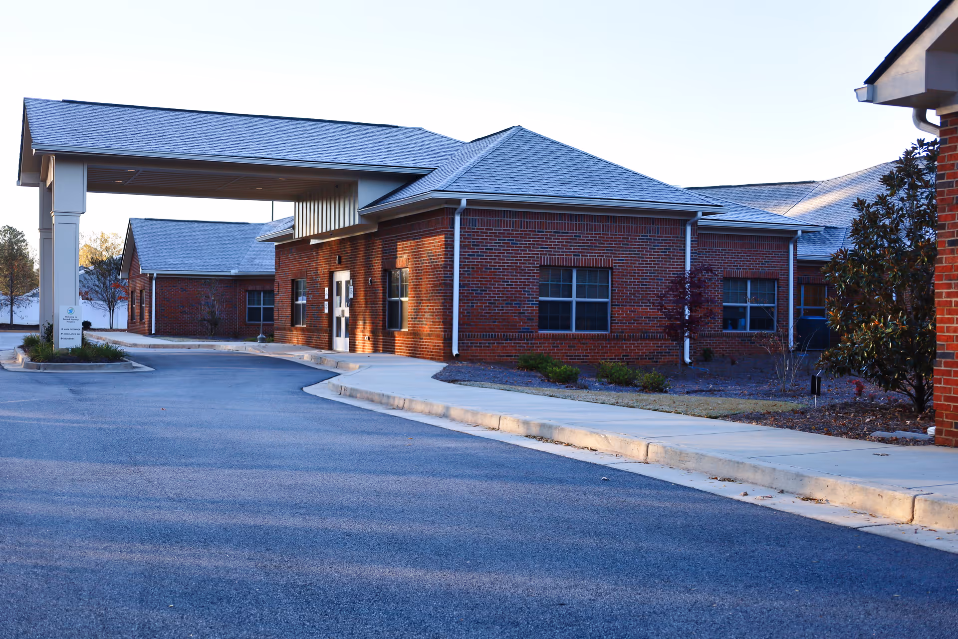 Brick hospice building with a covered entrance and paved driveway under a clear sky.